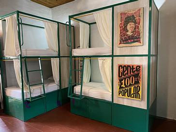 Viajero Hostels | Viajero Cali | Habitacion compartida con literas de metal verde con cortinas, lockers y arte grafica