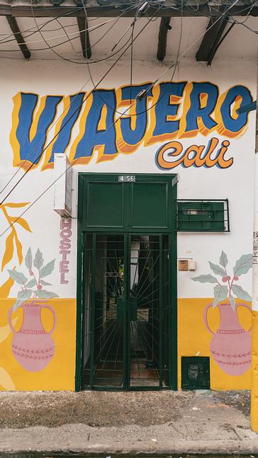 Viajero Hostels | Viajero Cali | Entrada con puerta verde y paredes con murales que lleva a Viajero Cali