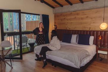 Viajero Hostels | Viajero Bogotá | Amigas en habitación privada tipo estudio con cama doble, mesita de cafe y balcón con vista a las montañas en el Hostal en Bogotá Viajero