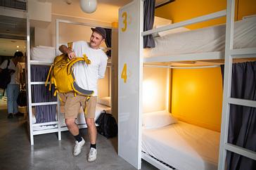 Viajero Hostels | Viajero Buenos Aires | Foreign tourist getting ready to leave in a shared dormitory with bunk beds and privacy curtains at Traveler Hostel Buenos Aires.