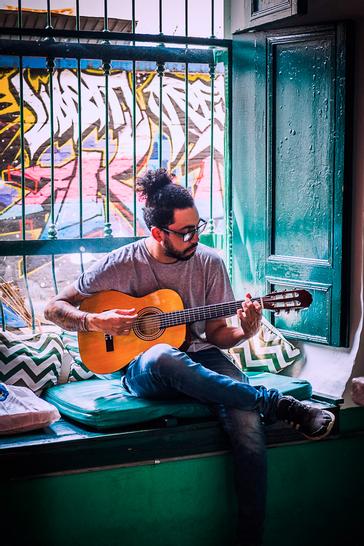 Viajero Hostels | Viajero Cali | Person sitting on a sofa while playing the guitar at Viajero Cali.
