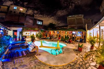 Viajero Hostels | Viajero Cali | Outdoor pool area at El Viajero Hostel Cali with a bar, volleyball net, and wooden loungers.