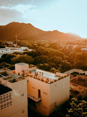 Viajero Hostels | Viajero Santa Marta | Vista de Santa Marta mostrando al naturaleza dentro de la ciudad y enfocando el rooftop con piscina en la cual grupo de personas disfrutan la vista