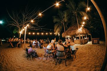 Viajero Hostels | Viajero Tayrona | Turistas, viajeros y amigos pasando la noche en el comedor de playa decorado con luces, disfrutando del ambiente relajante en viajero hostels Tayrona