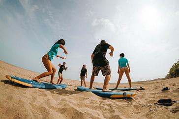 Viajero Hostels | Viajero Tayrona | Grupo de amigos aprendiendo a hacer surfing en un clase ofrecida por viajero hostel Tayrona en medio de la playa y jungla caribeña